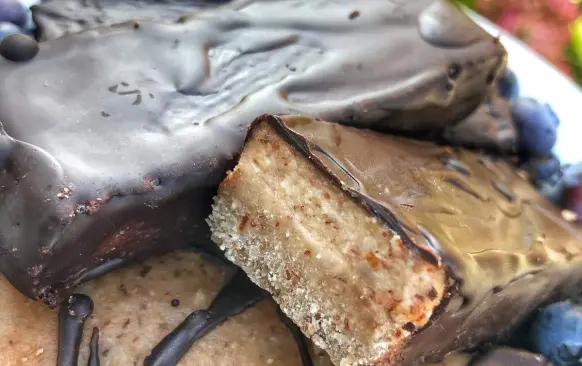 1. Nejdříve si připravíme první vrstvu. Mandle, kokosovou mouku a banán na první vrstvu rozmixujeme. Přimícháme kokosový olej. Vznikne nám těsto, které rozprostřeme do formy (velikost 22x9 cm) s pečicím papírem. Posypeme nasekanými oříšky, které do těsta lehce zatlačíme a dáme do mrazáku.

2. Mezitím si připravíme další vrstvu. Všechny ingredience na druhou vrstvu rozmixujeme, nalijeme na první vrstvu a dáme na 4 hodiny do mrazáku. Poté těsto rozřízneme na tyčinky, rozehřejeme hořkou čokoládu (asi 30-50 g) ve vodní lázni a obalíme tyčinky. Skladujeme v lednici.